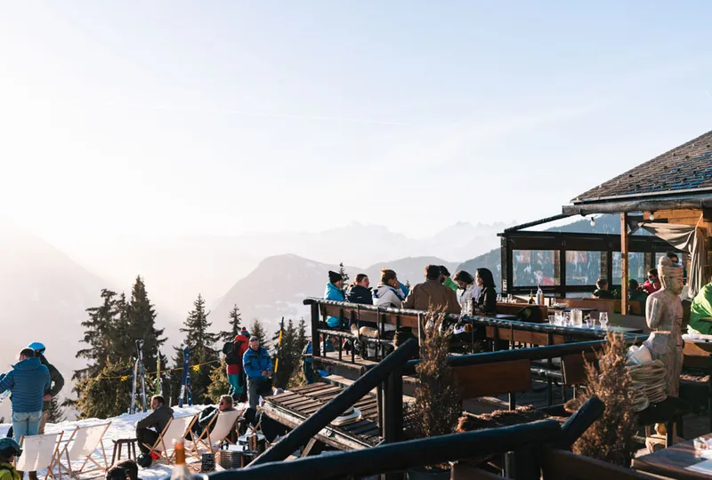 An outdoor terrace for apres ski has a few people seated under the late-day sun