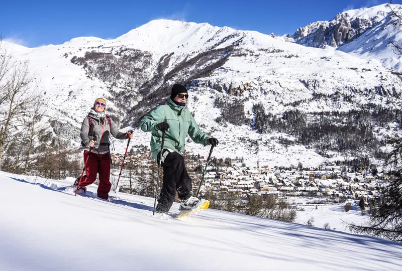 Two people snowshoeing through fresh powder, above the village