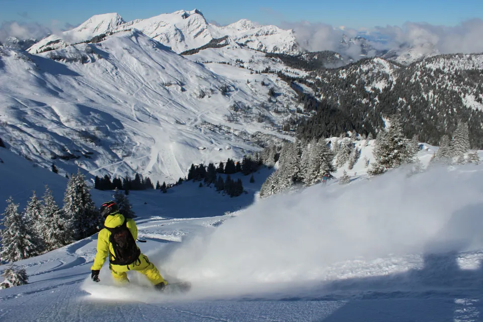 A snowboarder in yellow makes a turn and sprays snow in deep powder, off piste